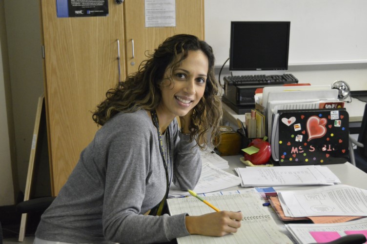 Confident looking teacher sitting at desk with pencil and paper."